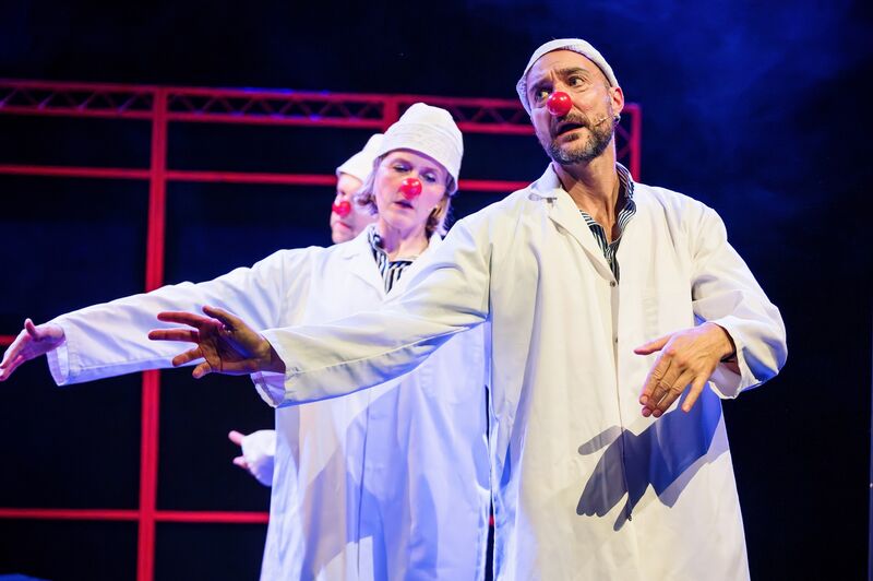 A row of three people wearing white coats, white hats and red clown noses, with their right arms outstretched